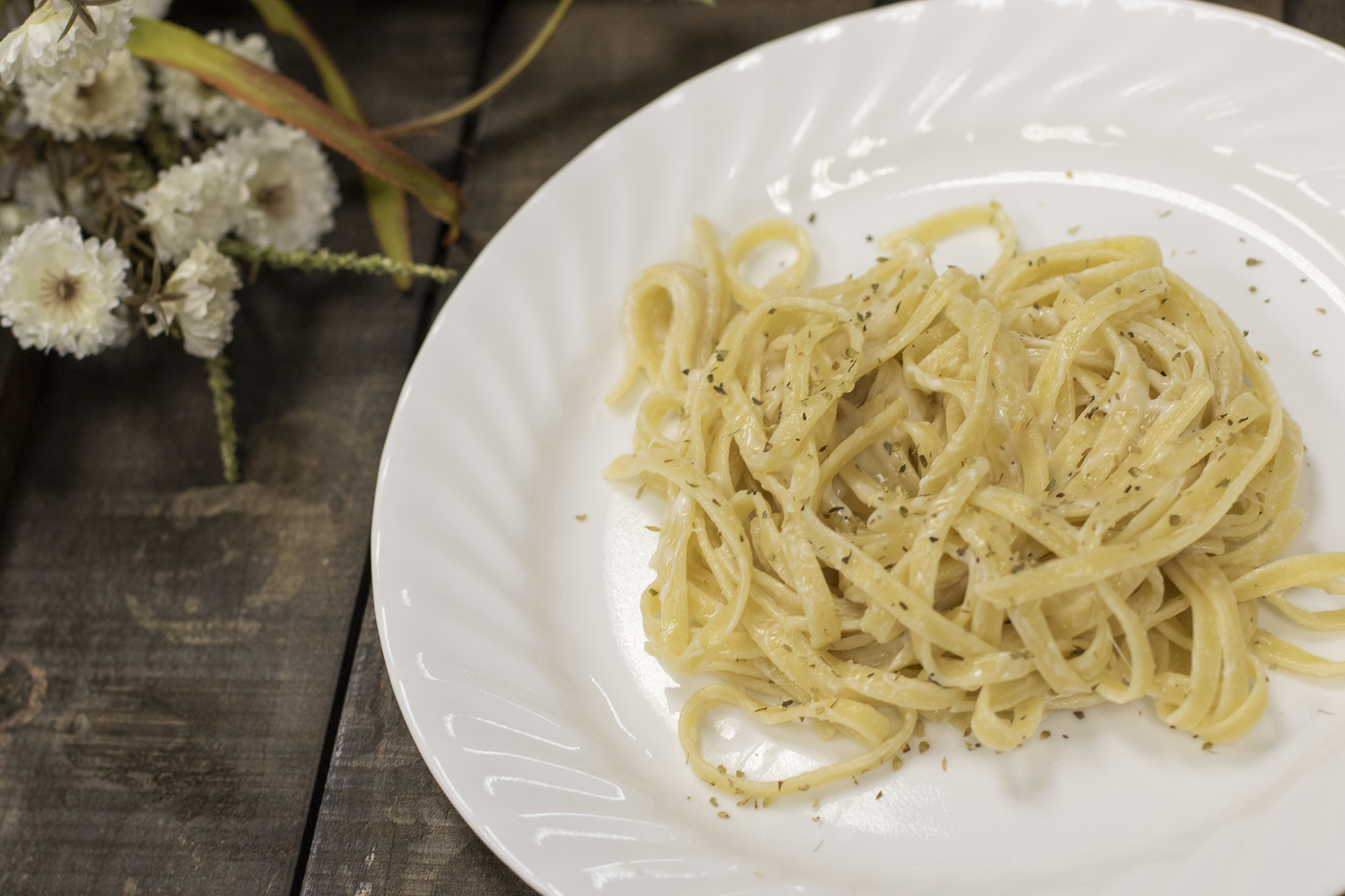 cottage cheese fettuccini Alfredo on a white plate surround by wood and white flowers.