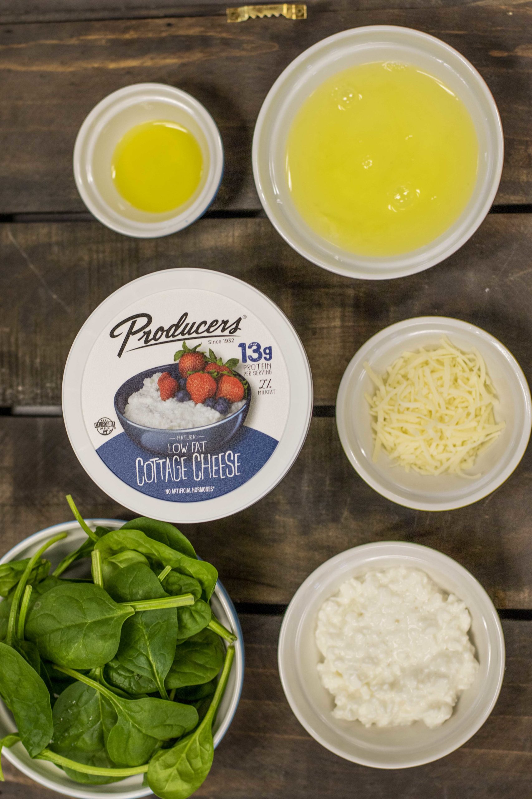 Producers Low Fat Cottage Cheese surrounded by spinach, oil, egg whites, and cheese on a wood table.