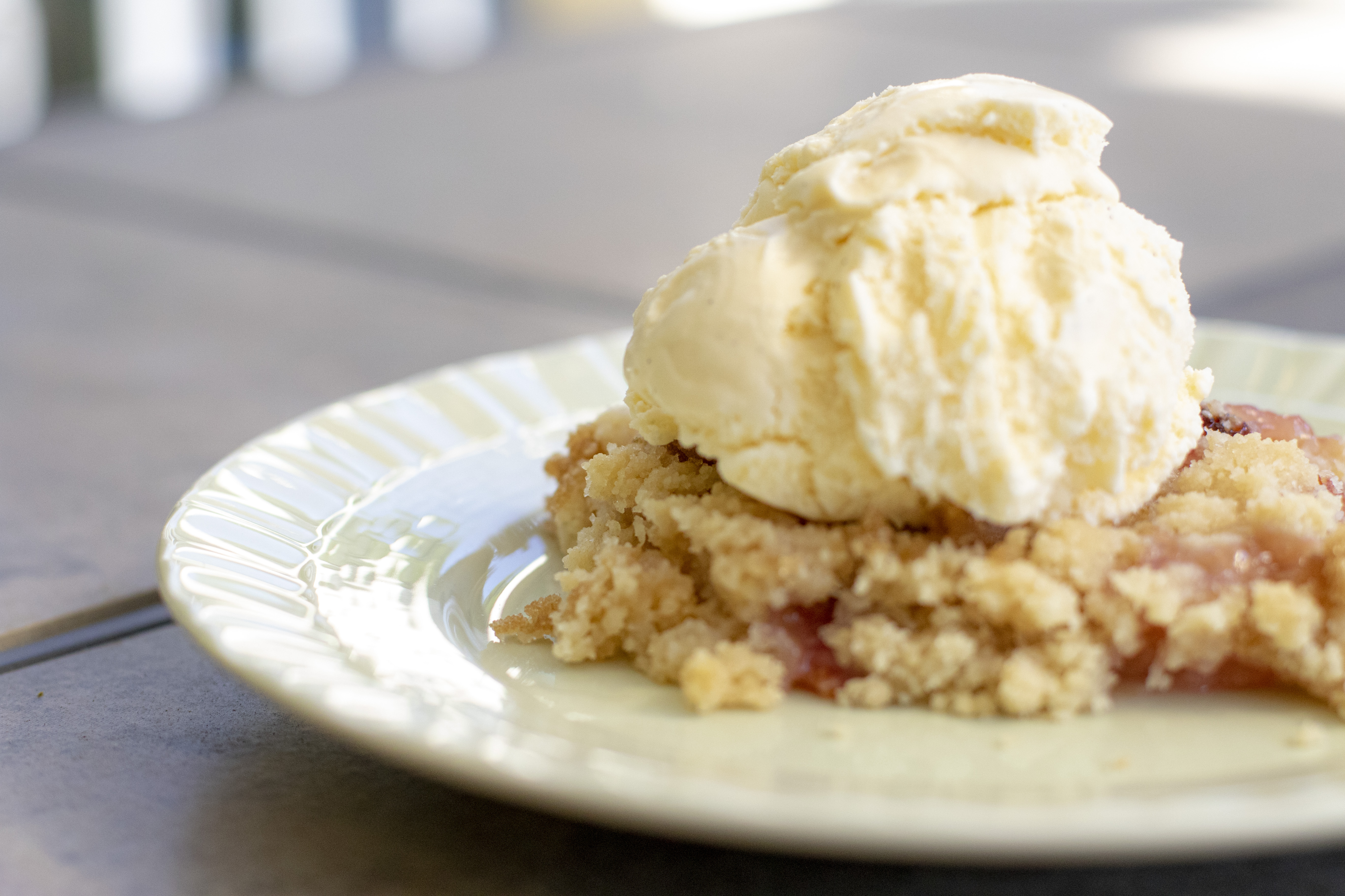 Peach cobbler on a green plate with vanilla bean ice cream on top outside on a patio table.