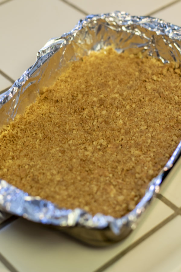 pumpkin cheesecake crust in a cooking pan with foil lining.