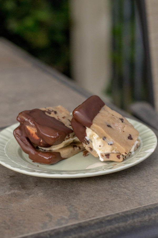 cookie dough ice cream sandwiches coated in chocolate on a green plate sitting on a patio table outside.