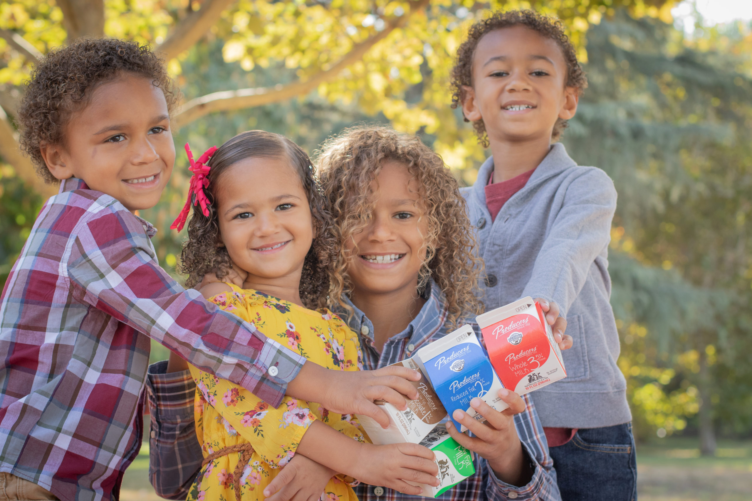 4 kids holding producers milk in the park.