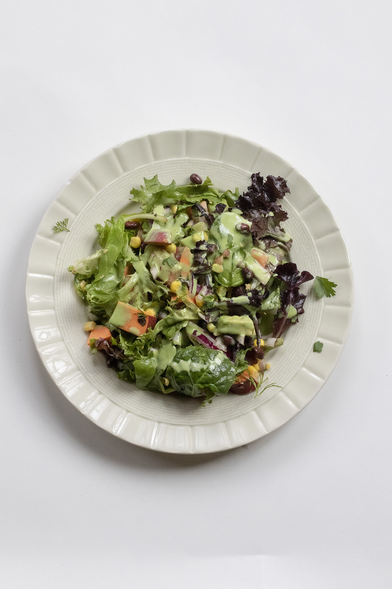 Southwestern salad with dressing on a green plate on a white background.