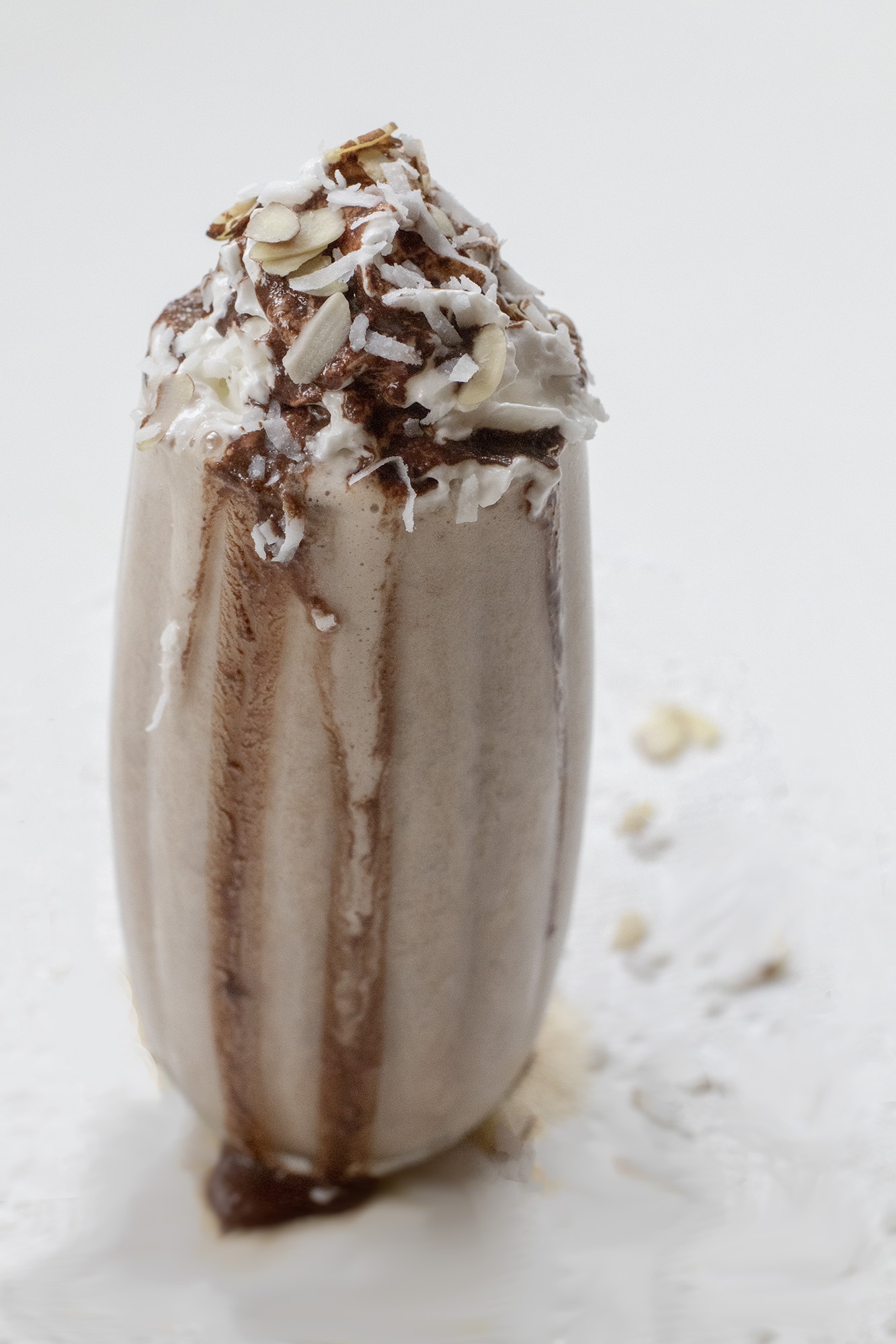 Chocolate Milkshake with whipped topping, sliced almonds, and shredded coconut on a white background.