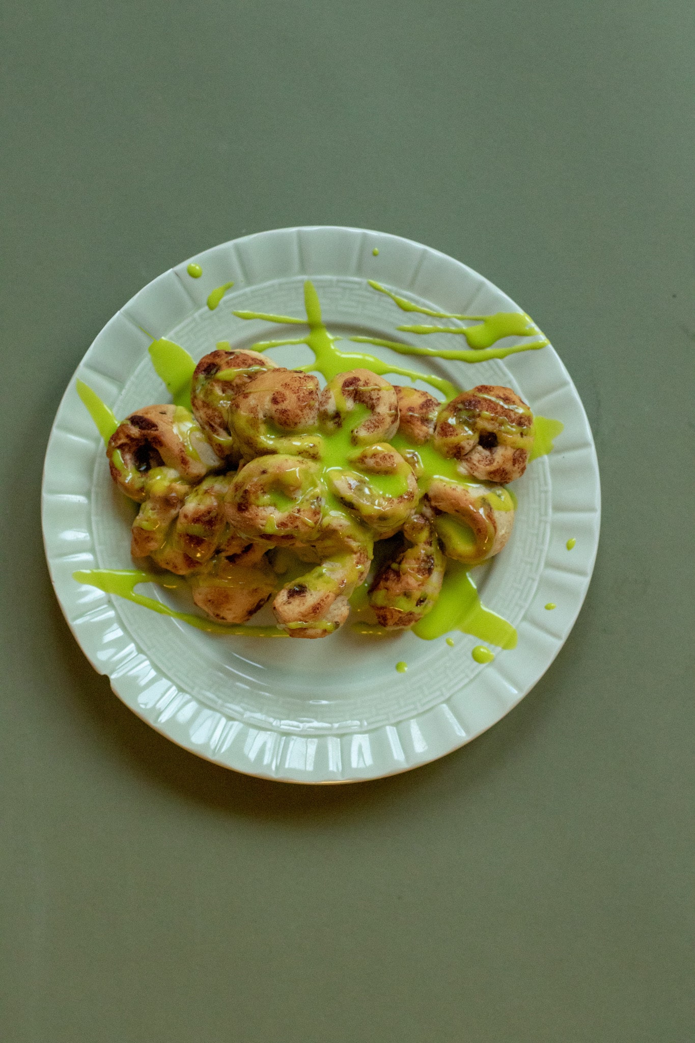 cinnamon rolls in the shape of four leaf clovers on a green plate with a green backdrop. Green frosting is spread all over the cinnamon rolls.