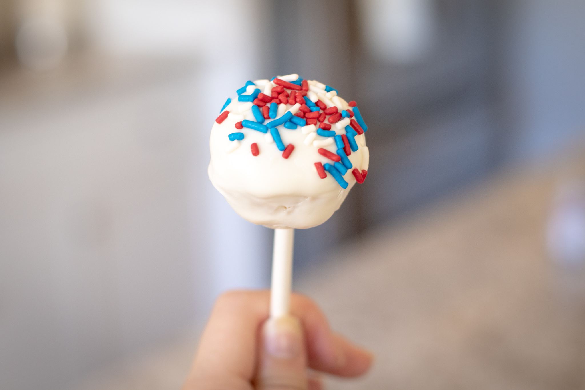 someone holding a cake pop with white chocolate and red white and blue sprinkles on it.
